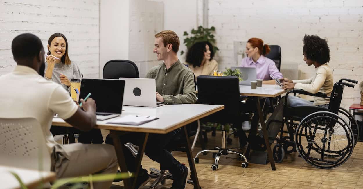 Multiracial team working together in a bright, modern office, showcasing diversity, inclusion, and collaboration in a professional environment, with a woman using a wheelchair